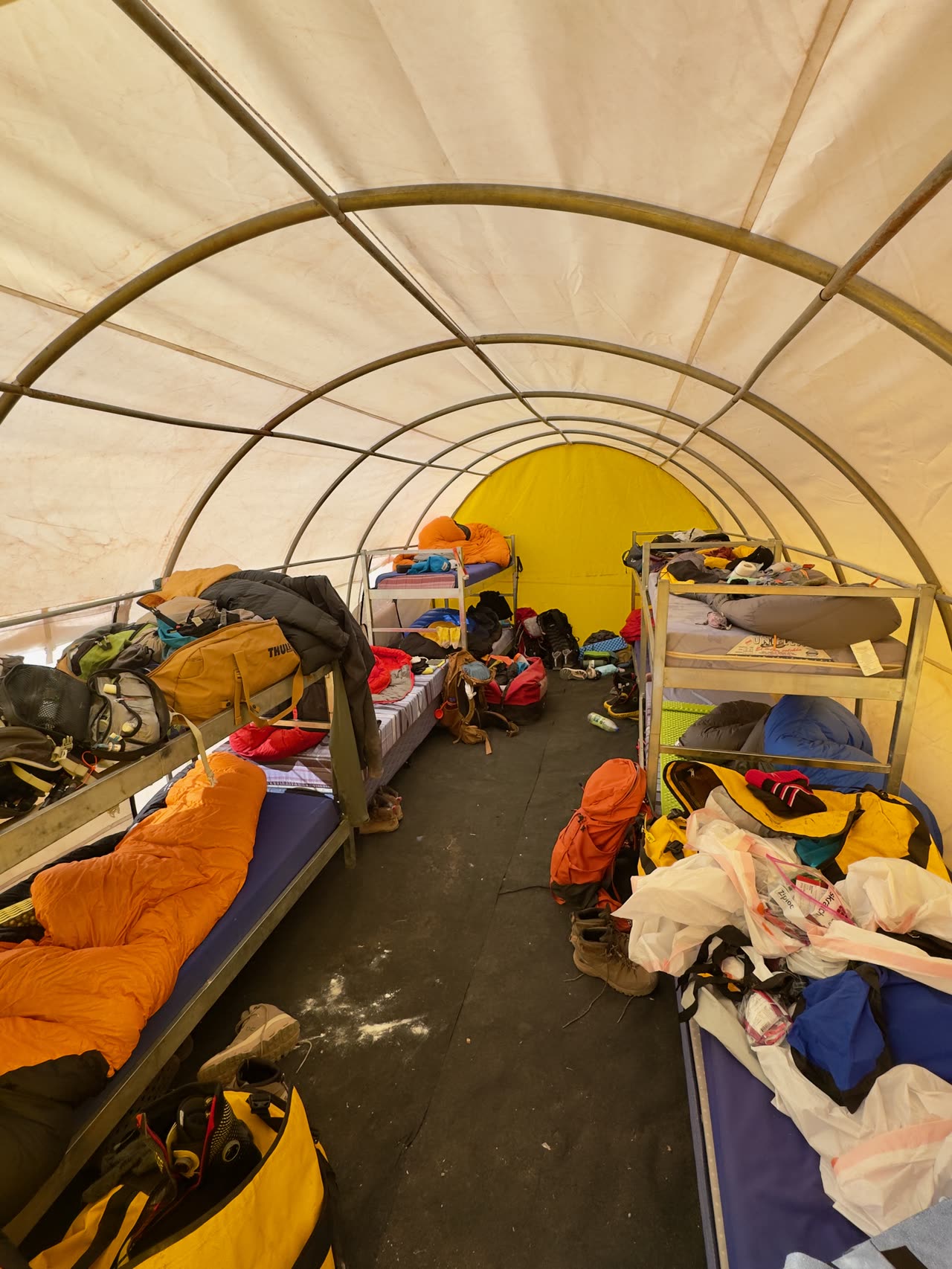 Interior of large yellow common tent with bunks and gear
