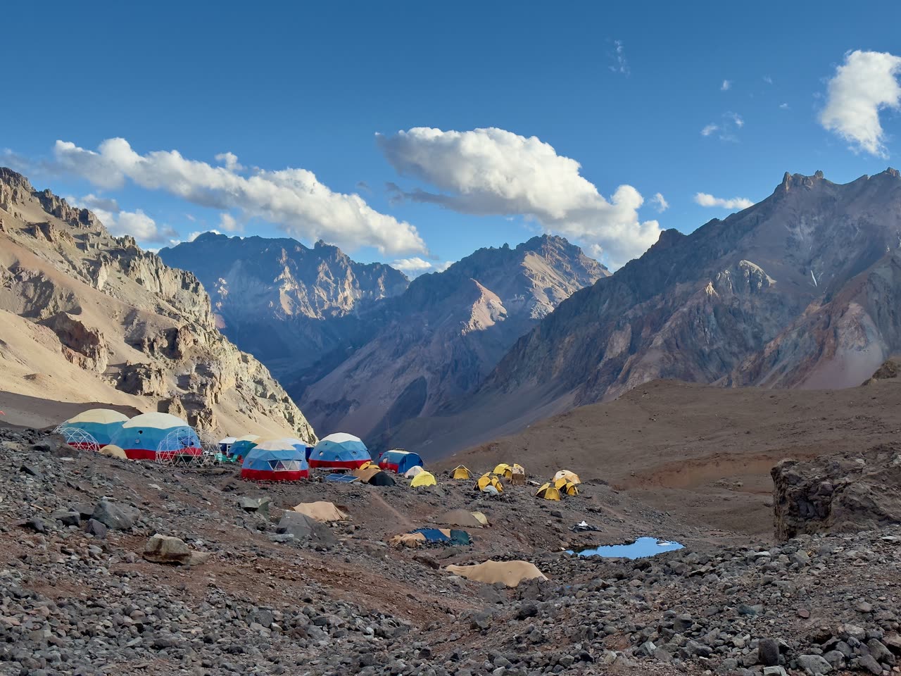 Base camp with colorful dome and tunnel tents against mountain backdrop