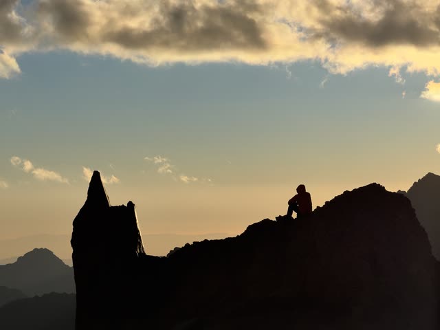 Silhouette of hiker sitting on rock at sunset
