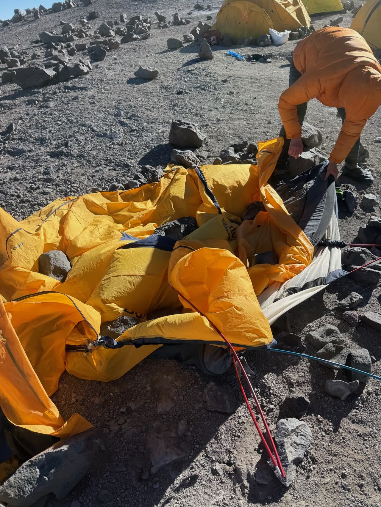 Yellow tent being set up on rocky ground